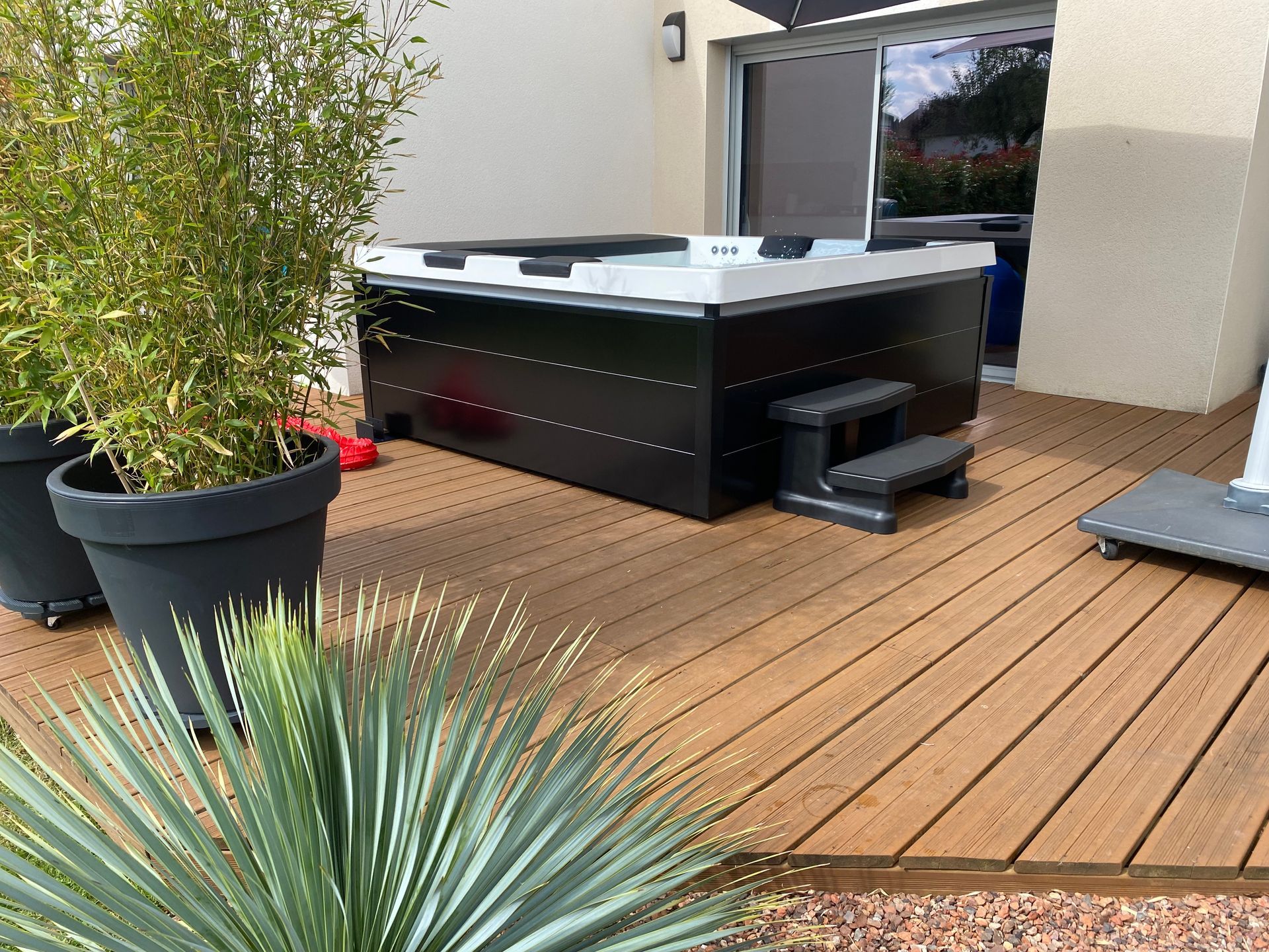 Un bain à remous est installé sur une terrasse en bois à côté de plantes en pot.