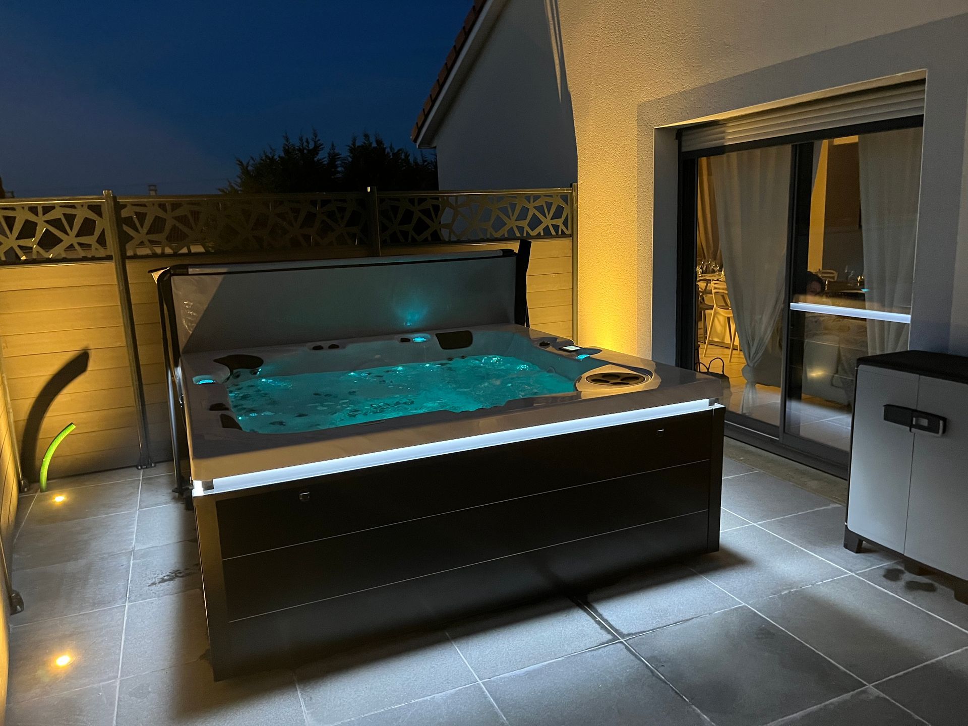 Un jacuzzi est éclairé la nuit sur une terrasse.