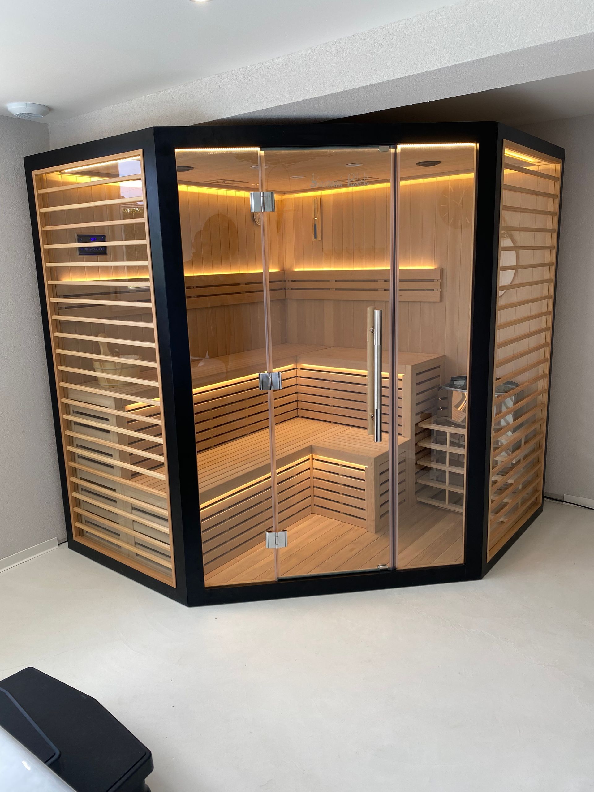Un sauna en bois avec une porte vitrée se trouve dans le coin d'une pièce.