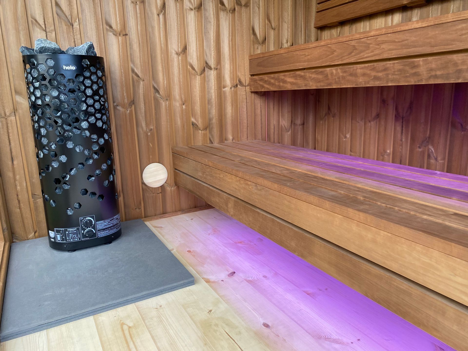 Un sauna en bois avec une lumière violette sur le sol.