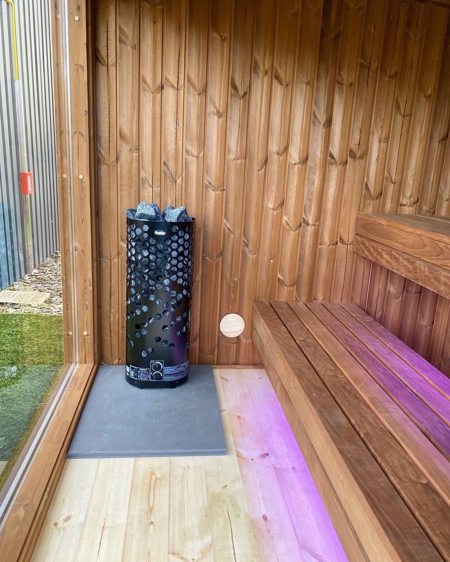 Un sauna en bois avec un poêle et des lumières violettes.