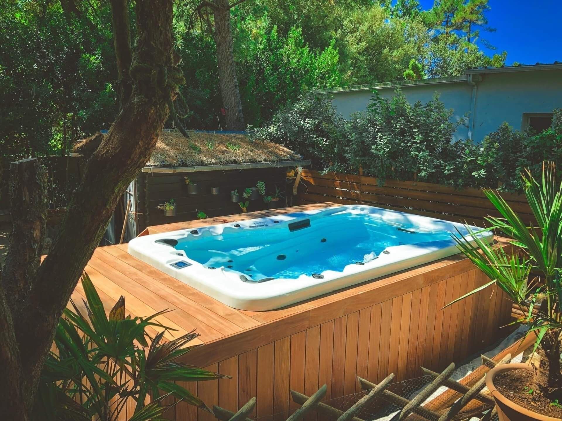 Un bain à remous est installé sur une terrasse en bois entourée d'arbres.