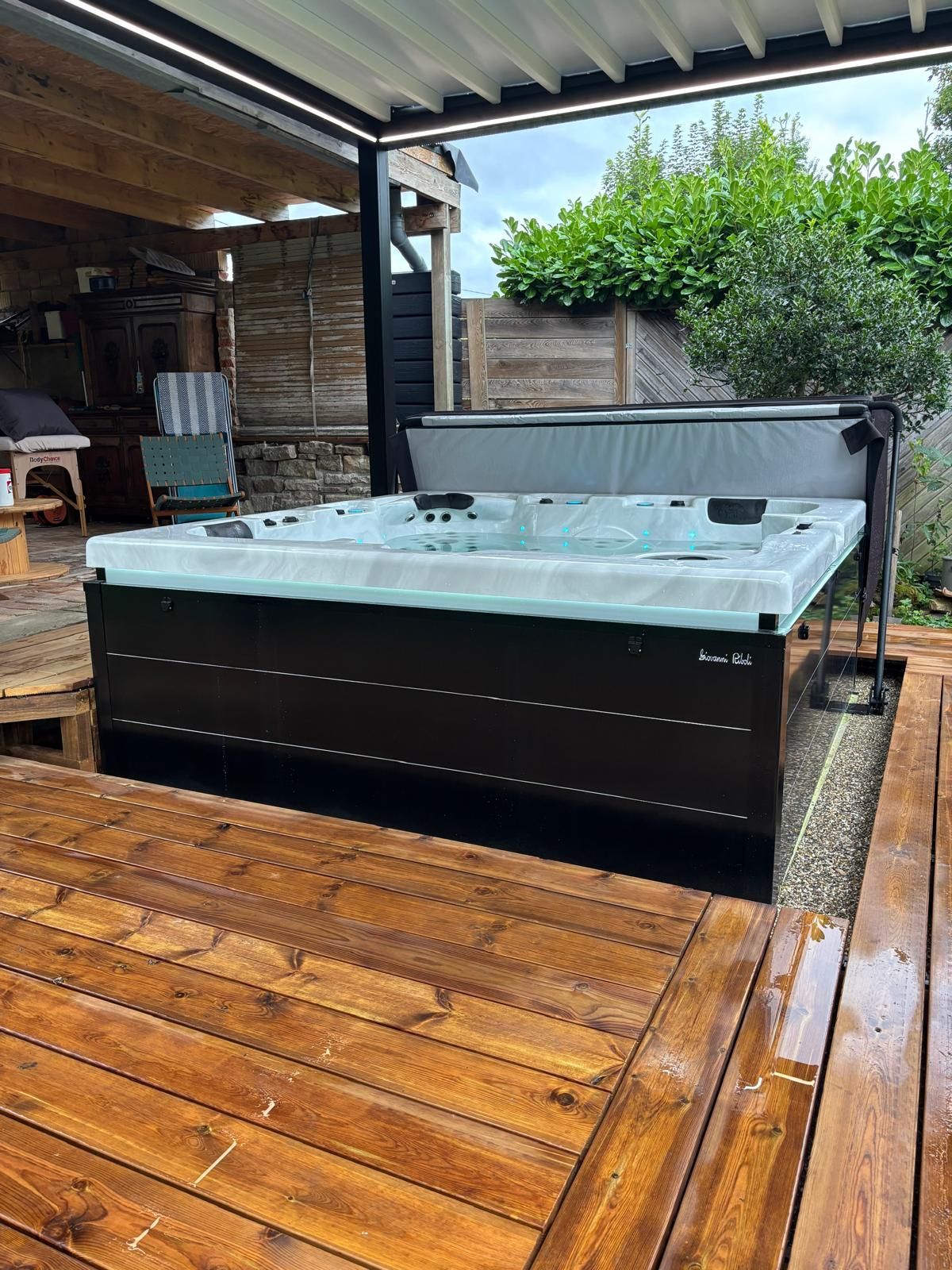 Spa sur une terrasse en bois sous un espace extérieur couvert. Baignoire noire avec couvercle gris.