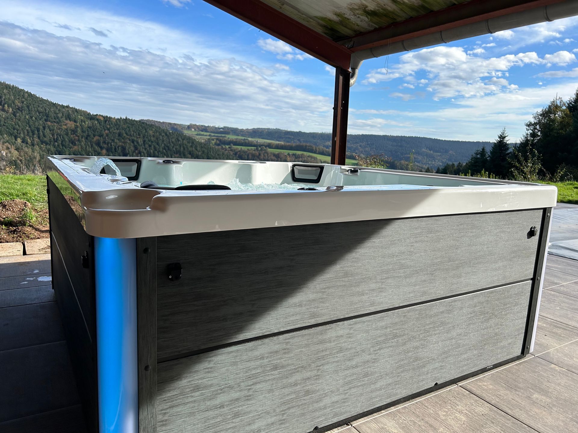 Un bain à remous est installé sous un auvent sur une terrasse avec des montagnes en arrière-plan.