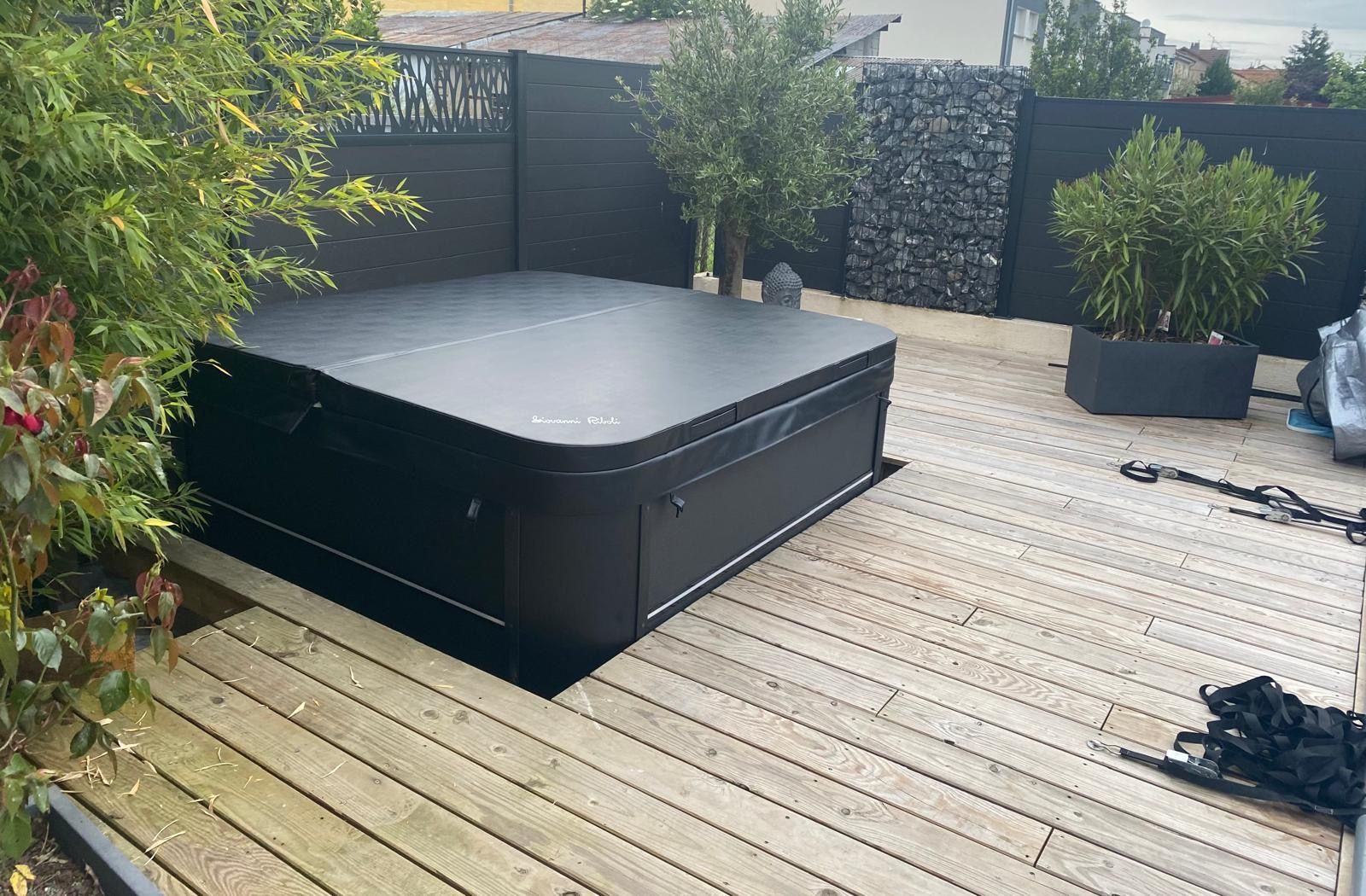 Un jacuzzi noir est posé sur une terrasse en bois.