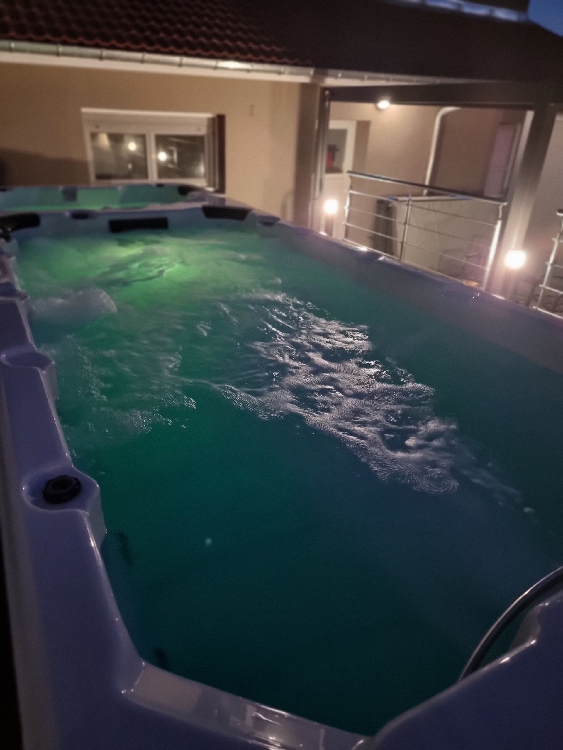 Une grande piscine est éclairée la nuit devant une maison.