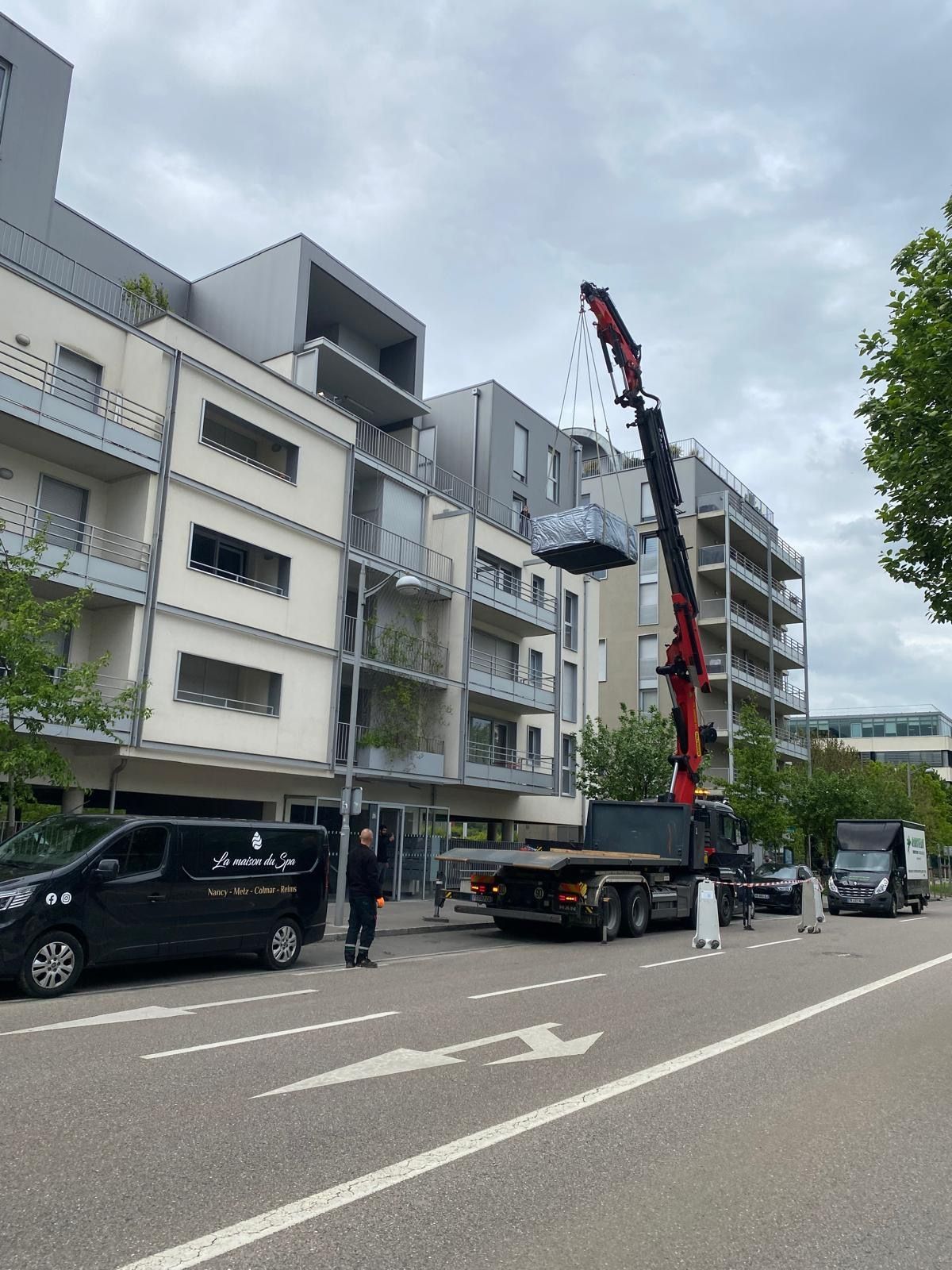 Un camion avec une grue à l'arrière est garé sur le bord de la route devant un bâtiment.