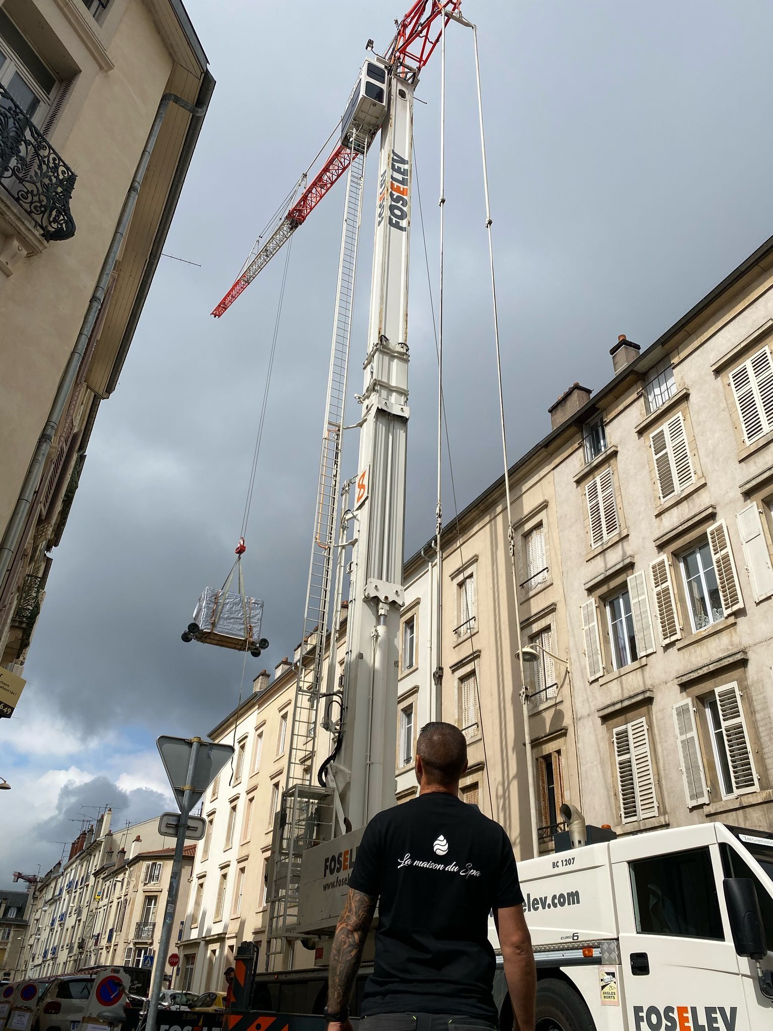 Un homme se tient devant une grande grue dans une ville.