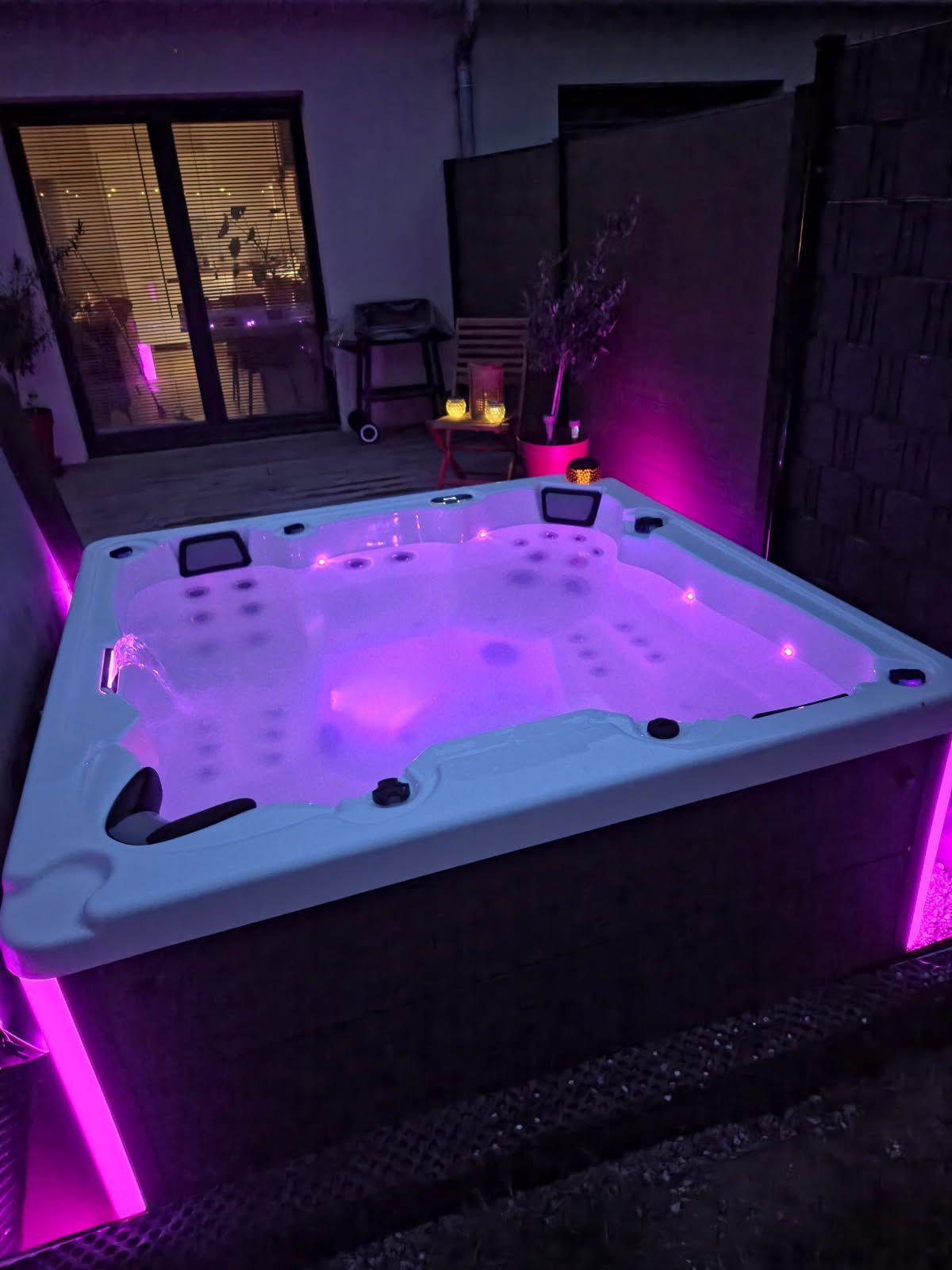 Un bain à remous éclairé brille en violet la nuit dans une cour arrière.