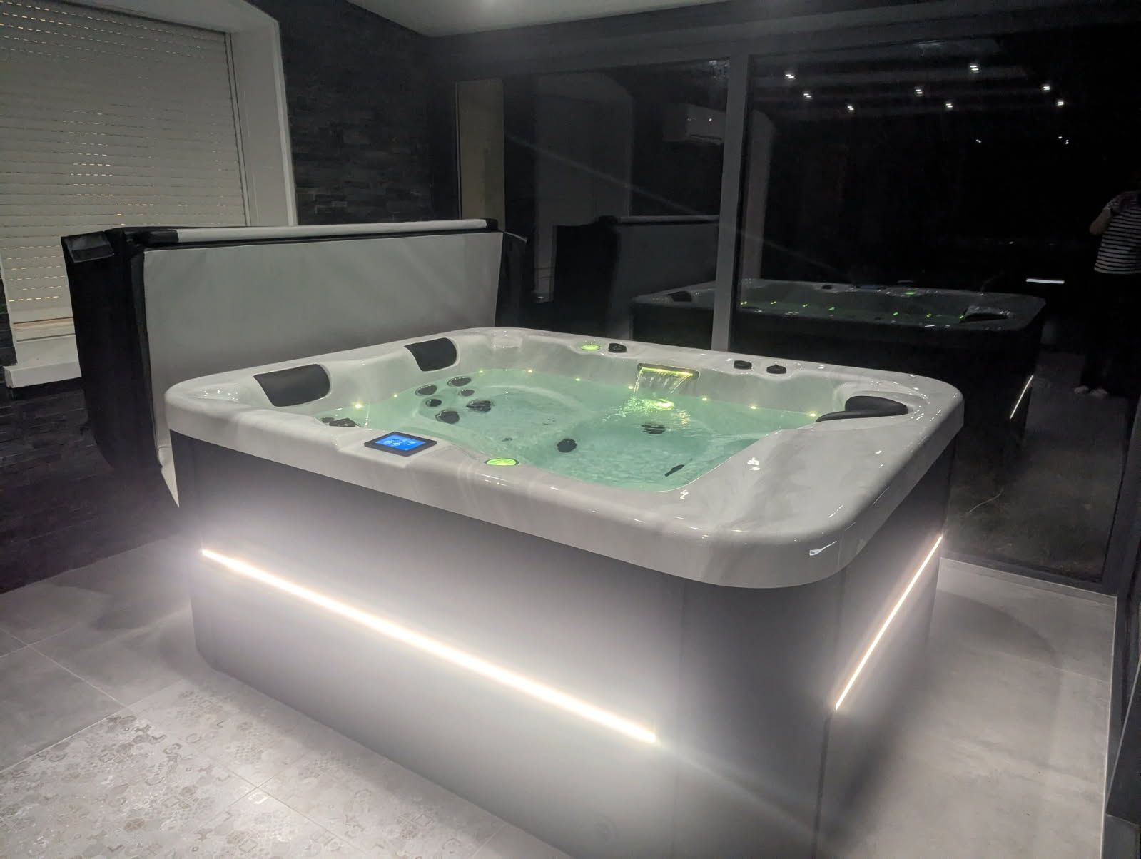 Un jacuzzi éclairé dans une pièce, avec un autre en arrière-plan. Les couleurs dominantes sont le blanc, le gris et le noir.