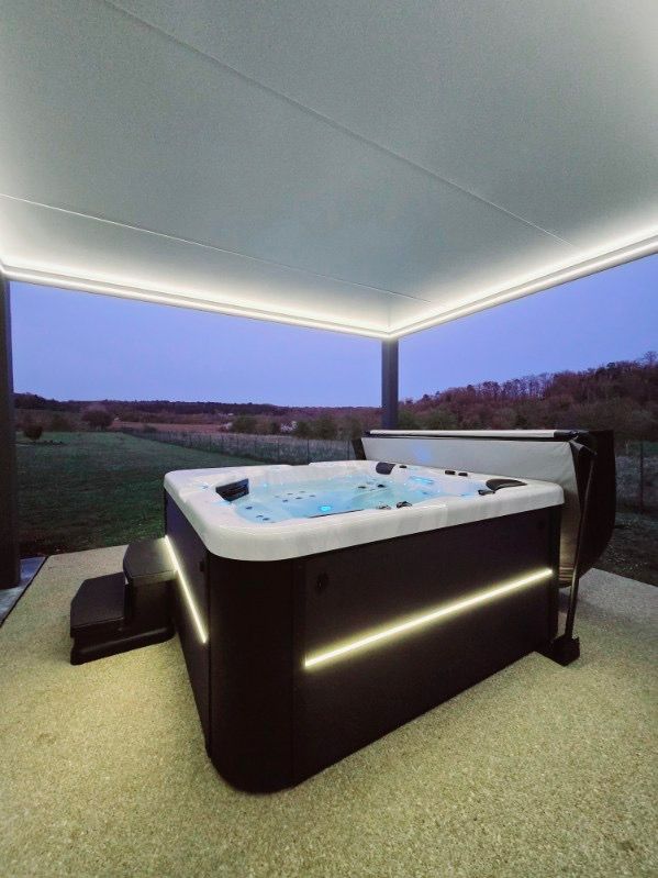Un bain à remous est installé sous une pergola avec vue sur un champ.
