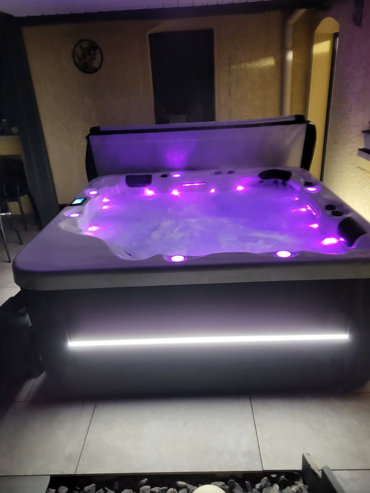 Spa éclairé avec des lumières violettes et une bordure blanche brillante, à l'extérieur la nuit.
