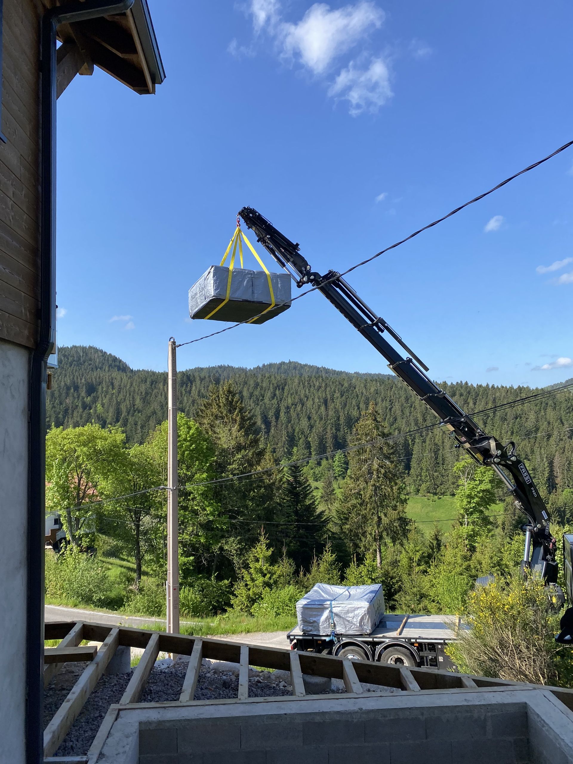 Une grue soulève un objet volumineux au-dessus d'un bâtiment.