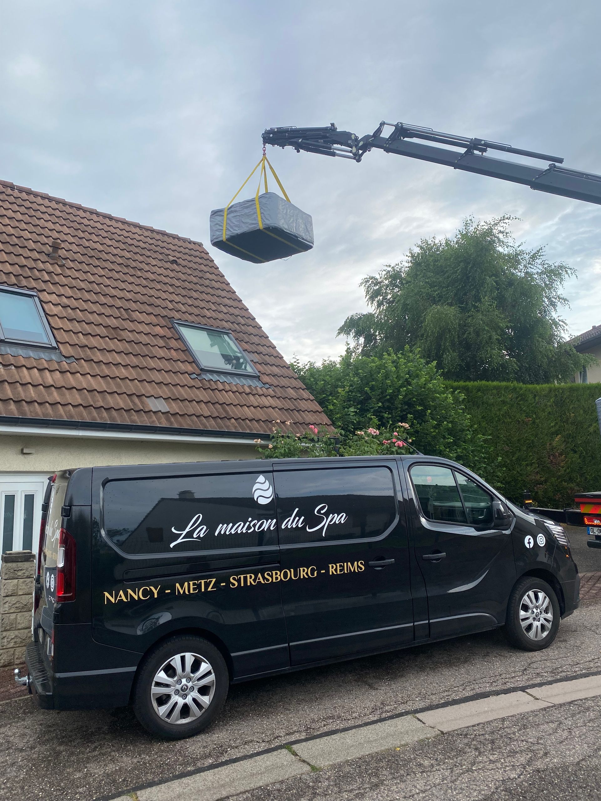 Une camionnette noire est garée devant une maison avec une grue soulevant une boîte du toit.