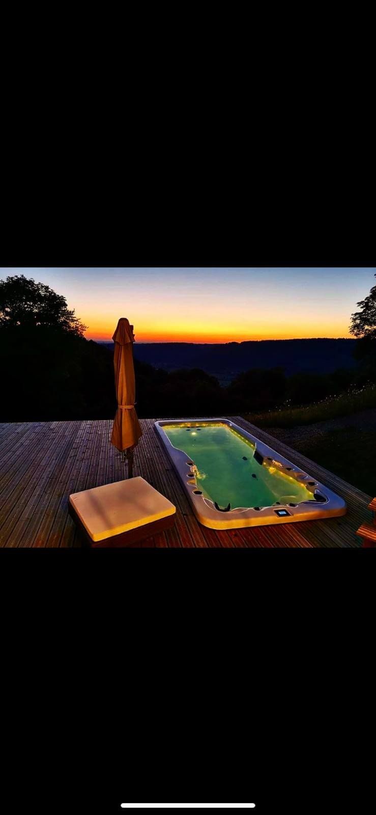Une grande piscine est éclairée la nuit avec un coucher de soleil en arrière-plan.