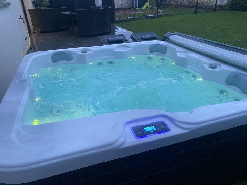 Un jacuzzi blanc est posé sur une pelouse verte luxuriante.