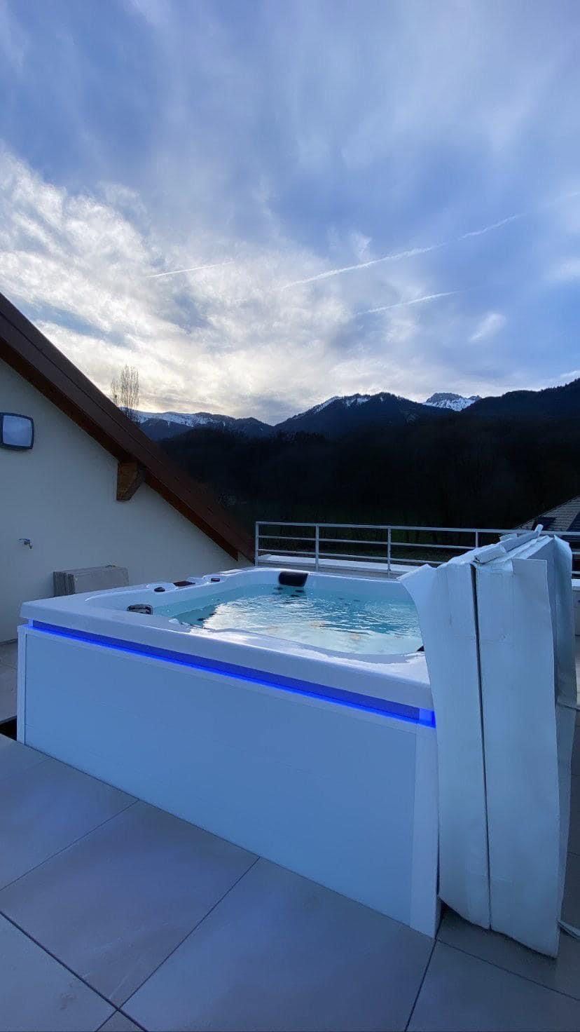 Un grand jacuzzi blanc est posé au sommet d'un patio avec des montagnes en arrière-plan.