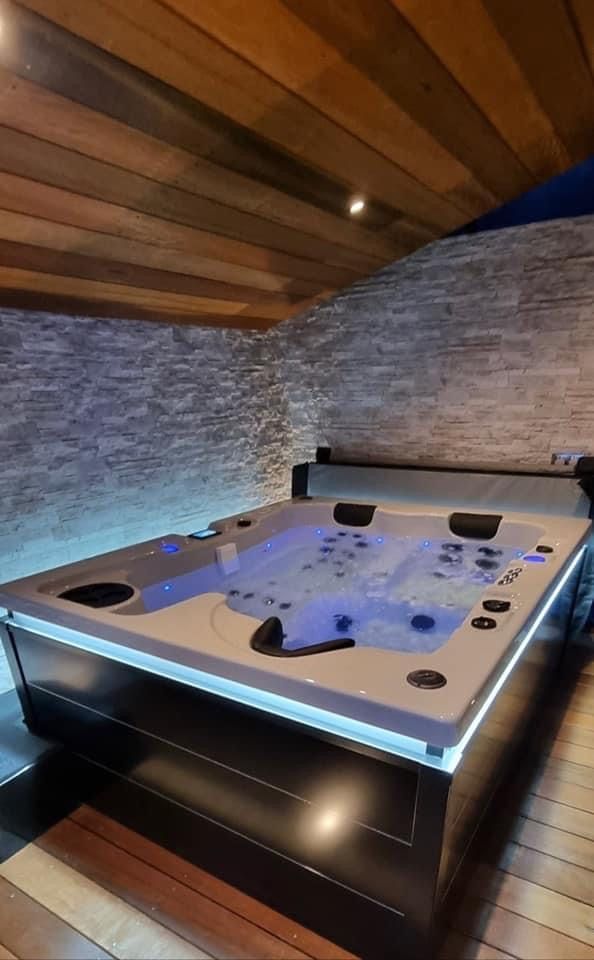 Un grand bain à remous est posé sur un plancher en bois dans une pièce.