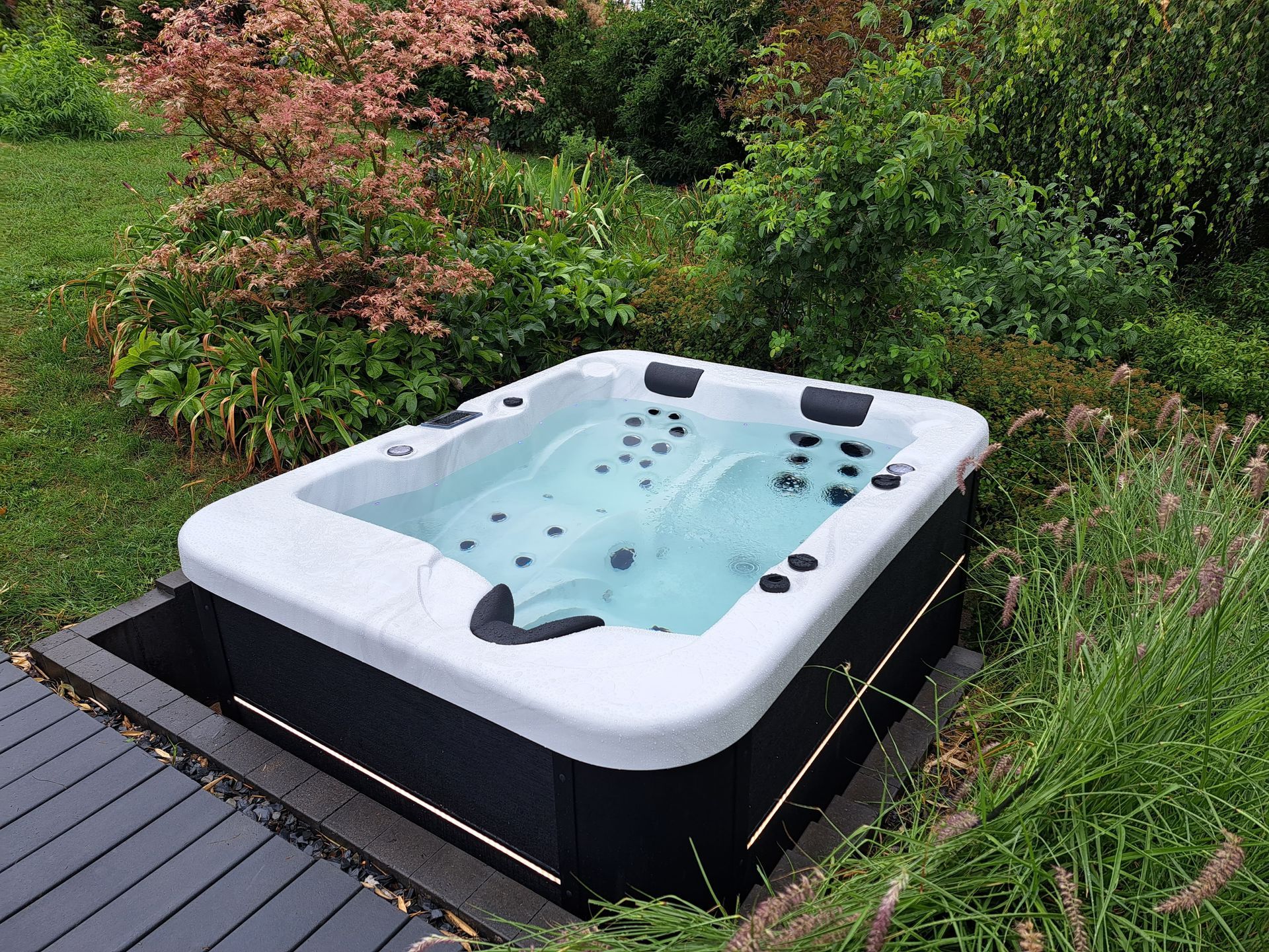 Un bain à remous est installé sur une terrasse en bois au milieu d'un jardin.