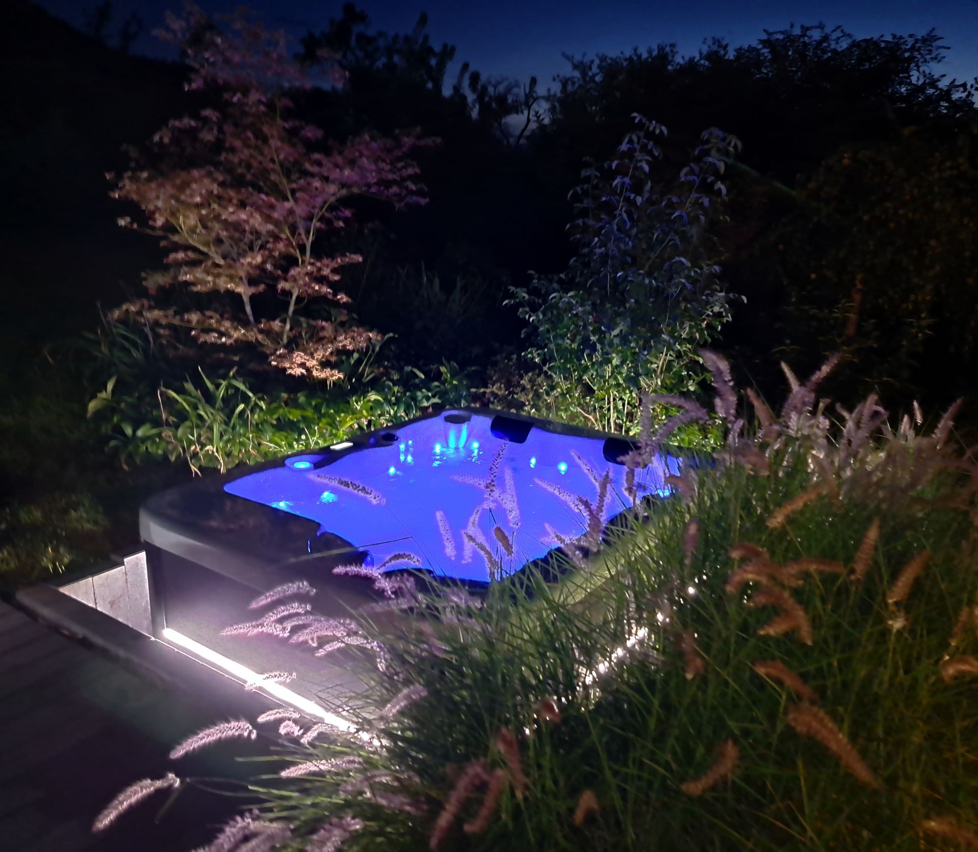 Un jacuzzi est éclairé la nuit dans un jardin