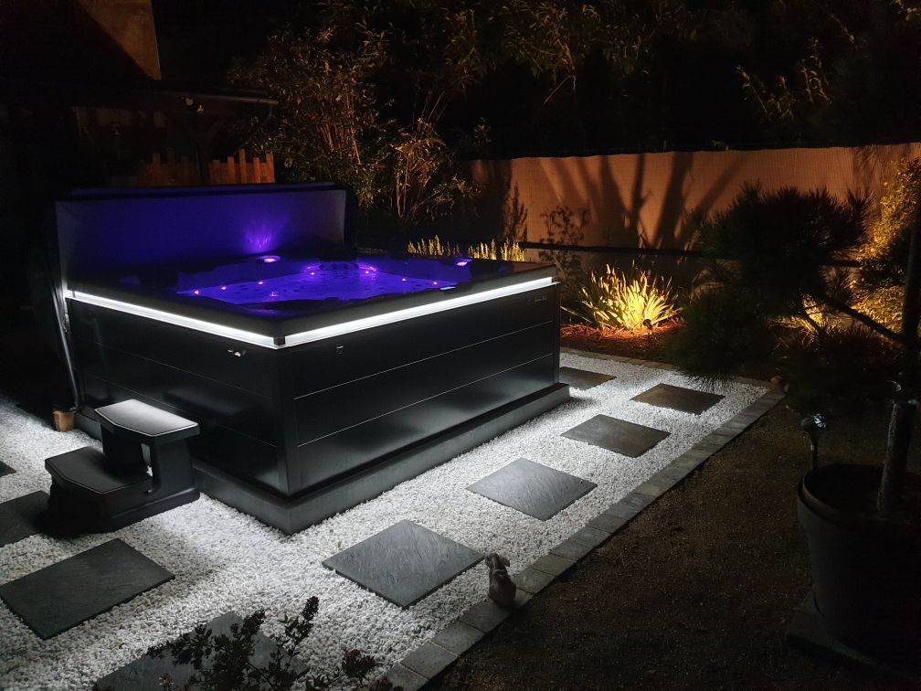 Un jacuzzi noir est éclairé la nuit dans une cour arrière.