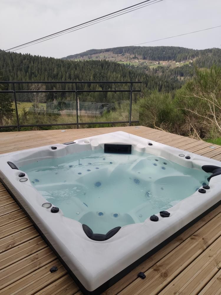 Un bain à remous est posé sur une terrasse en bois avec des montagnes en arrière-plan.