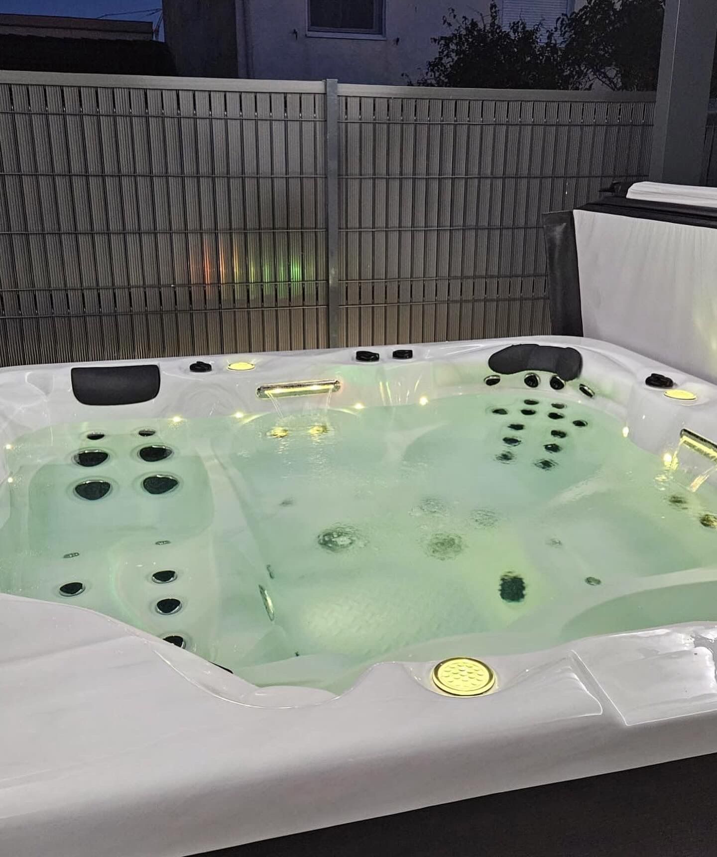 Un jacuzzi blanc avec de l'eau verte est assis devant une clôture.