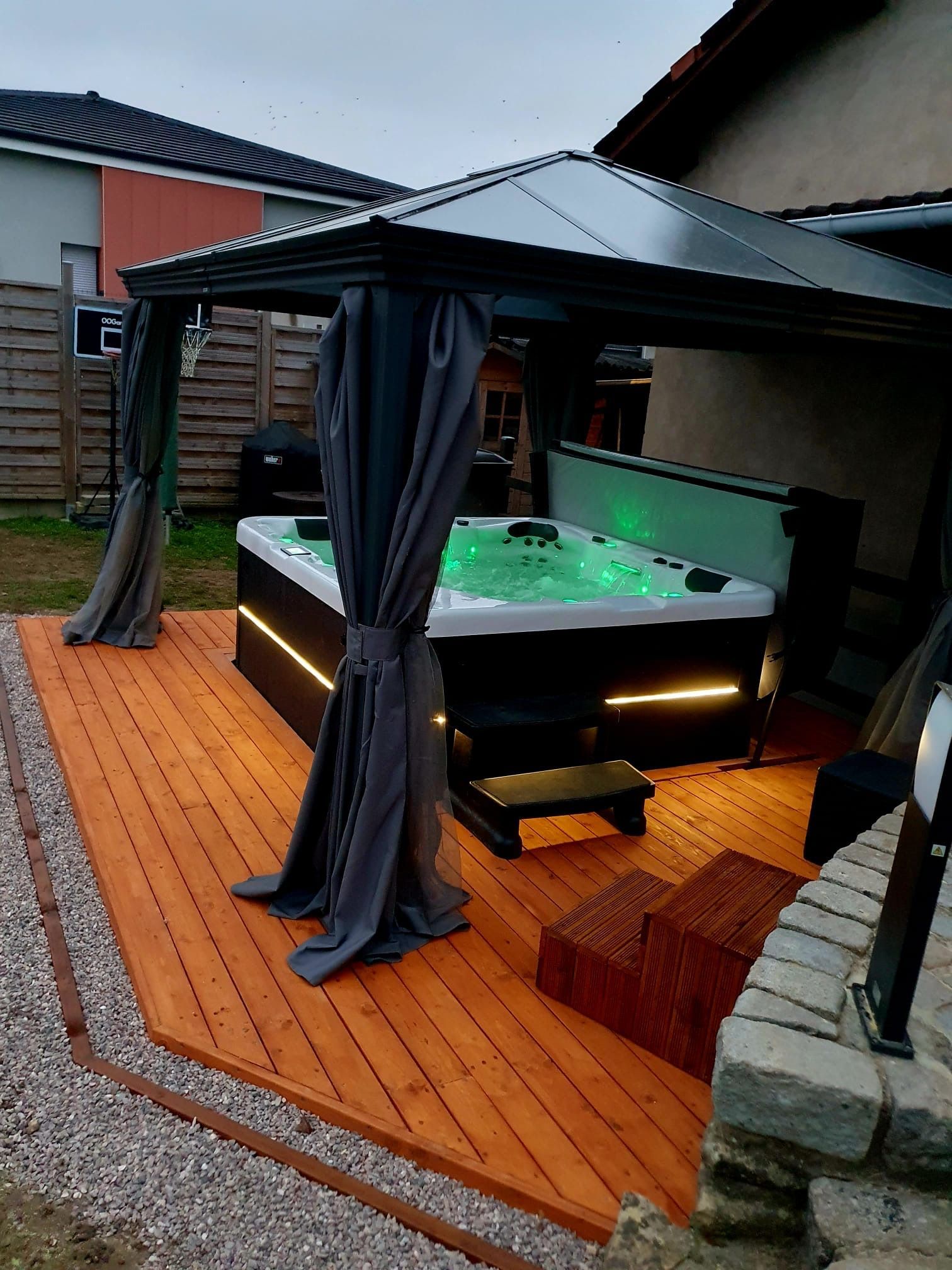 Un bain à remous est installé sous un auvent sur une terrasse en bois.