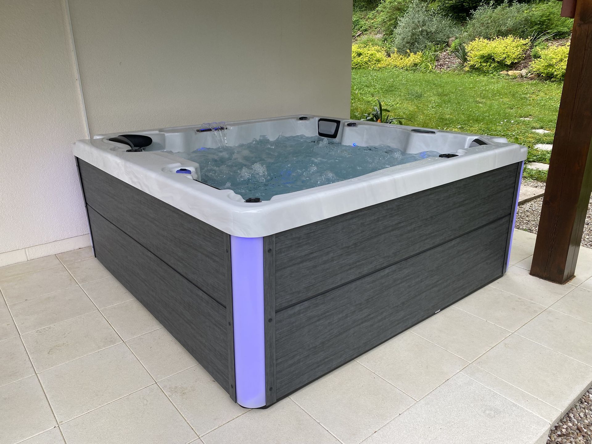 Un jacuzzi gris et blanc est posé sur un patio carrelé.