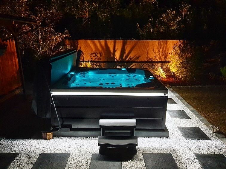 Un jacuzzi noir est éclairé la nuit dans une cour arrière.