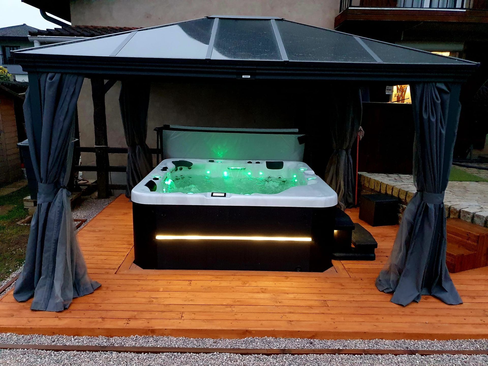 Un bain à remous est installé sous un gazebo sur une terrasse en bois.
