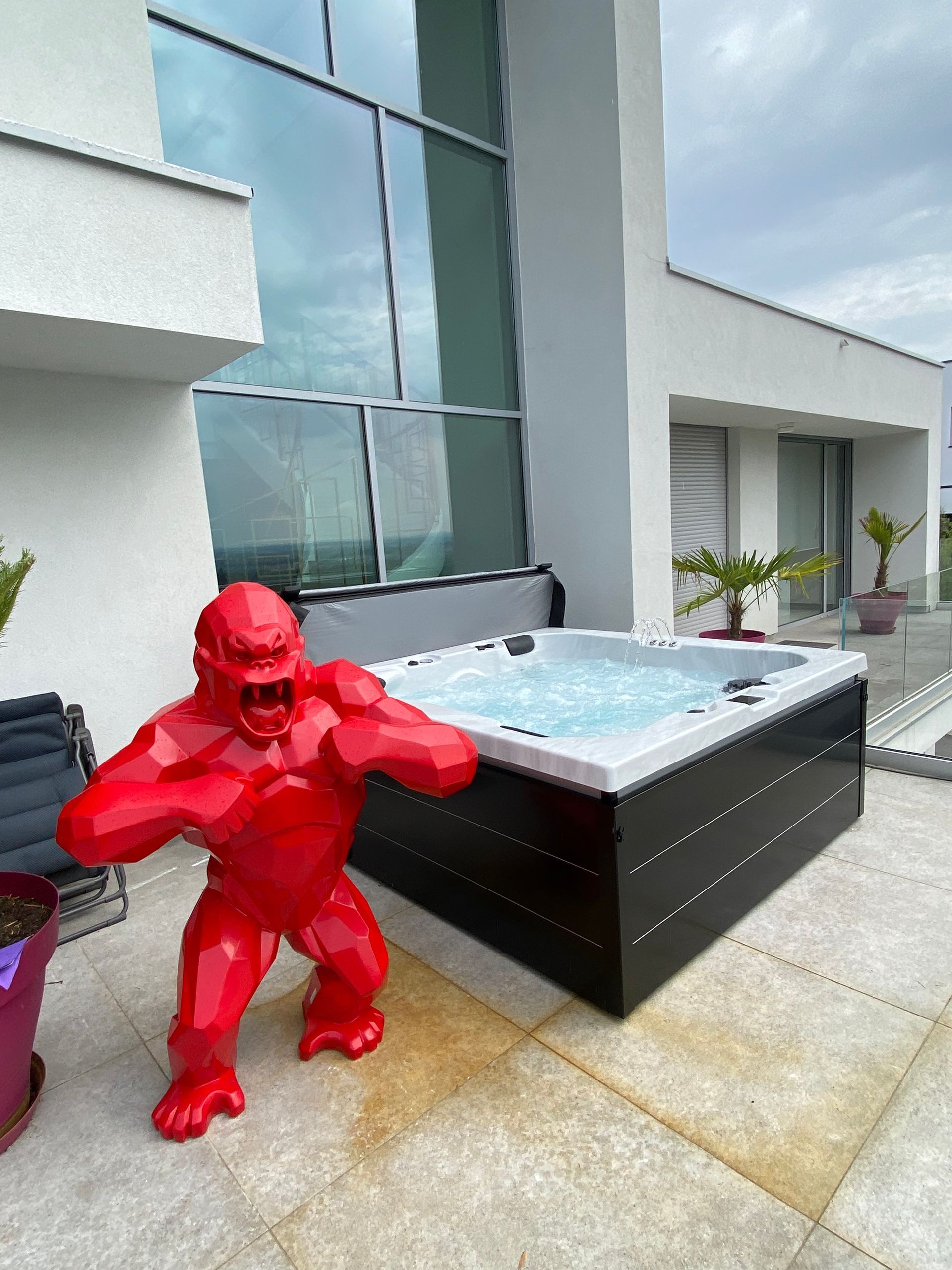 Une statue de gorille rouge se tient à côté d'un bain à remous sur une terrasse.