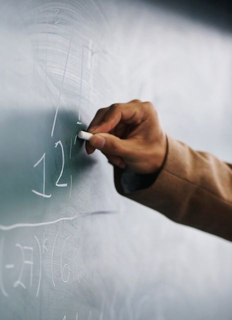 Cropped image of a teacher writing a formula on a blackboard