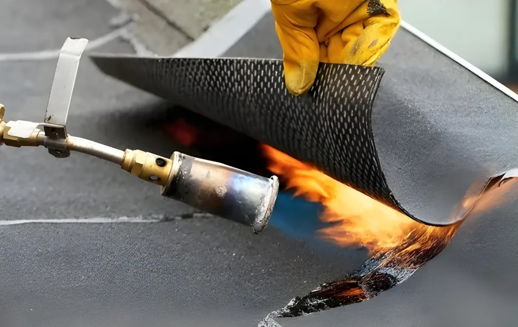 Roofer kneels on a flat roof, orange shirt, hard hat, sunny day, working with tools.