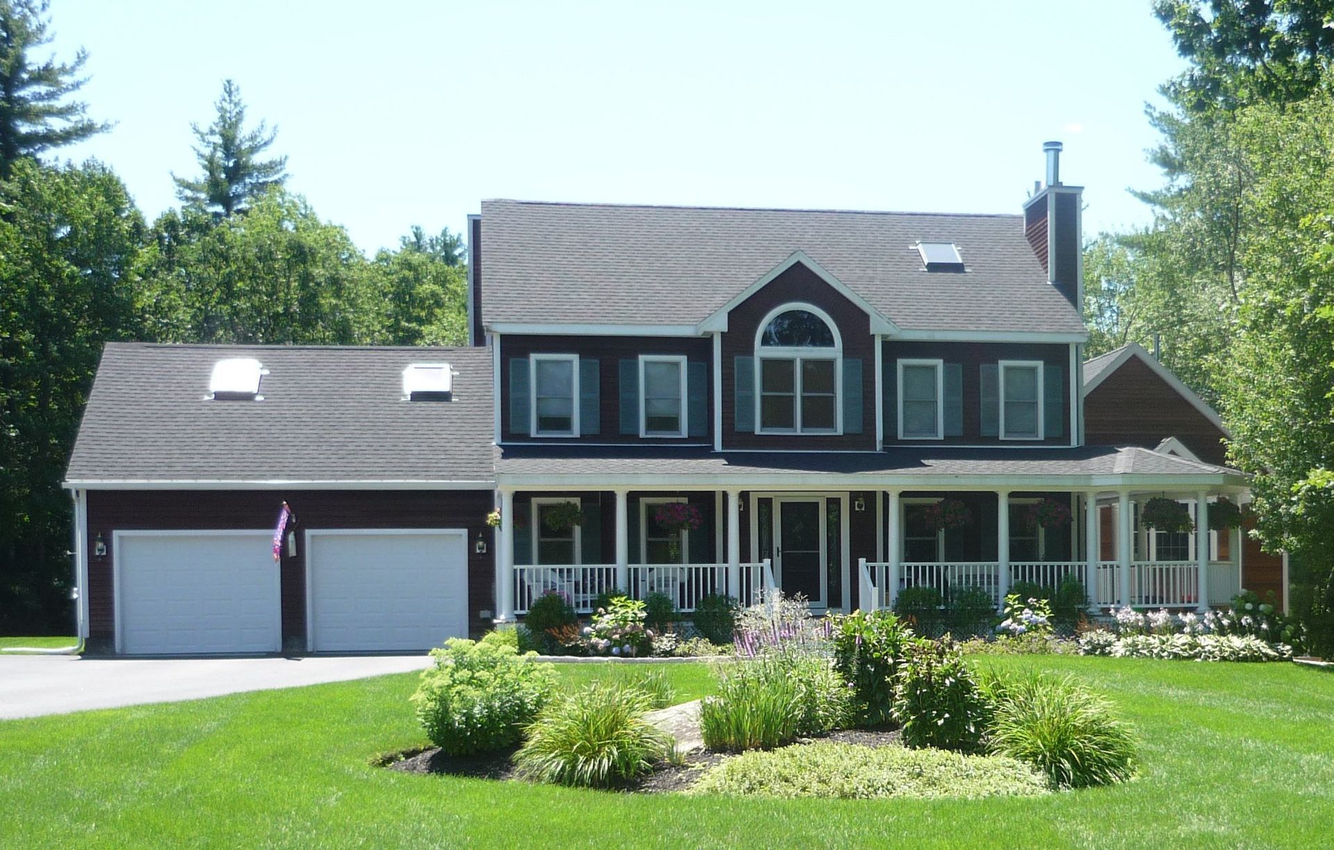 Two-story dark house with white trim, porch, and attached garage on a green lawn.