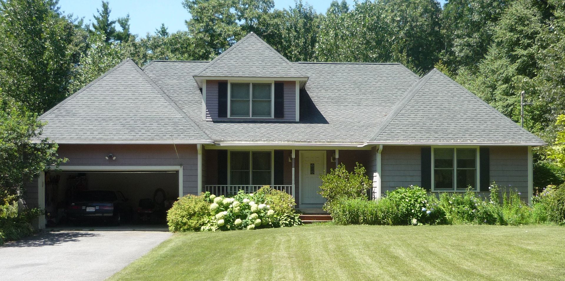 House with gray roof, garage, and yard surrounded by trees.