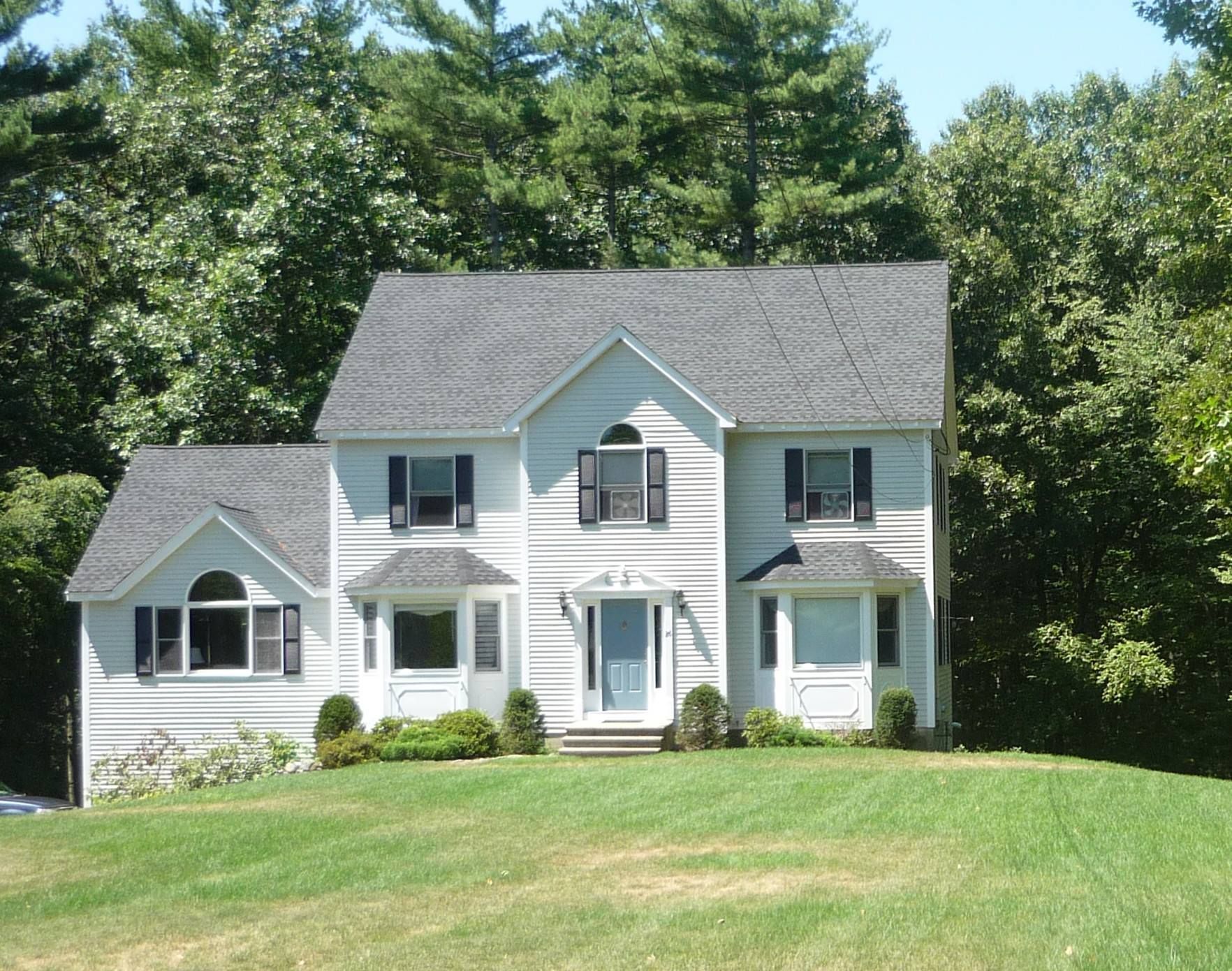 Two-story white house with gray roof and black shutters, set in a grassy yard, with trees in the background.