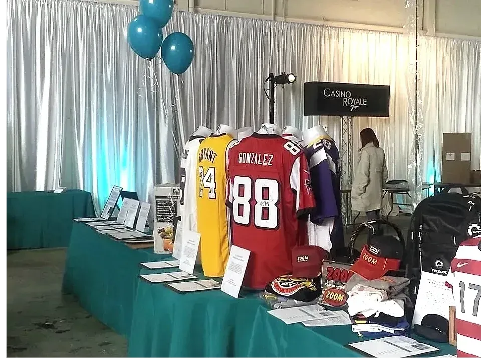 Table display of sports jerseys and merchandise at an event, with teal table cloth and balloons.