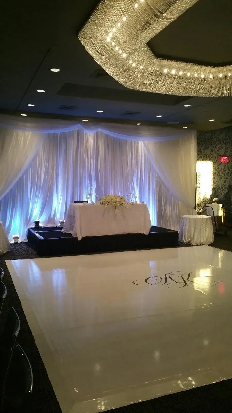Wedding reception setup with white dance floor, draped backdrop, and decorated table.