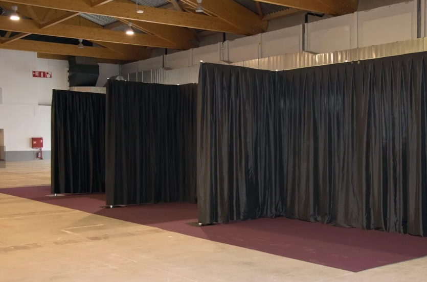 Black curtain dividers set up in a large hall with a concrete floor and wood beam ceiling.