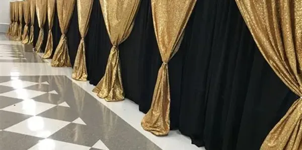 Black and gold draped table skirt in a room with checkered floor.