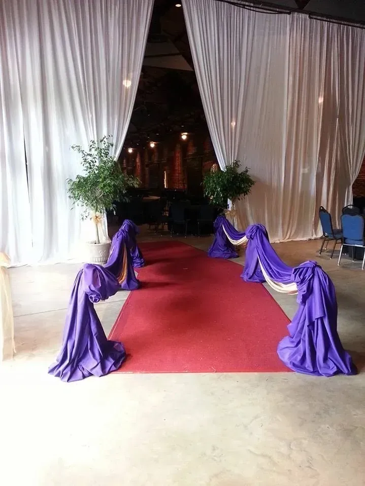 Red carpet aisle with purple draped fabric leading to an event entrance, flanked by white curtains and greenery.