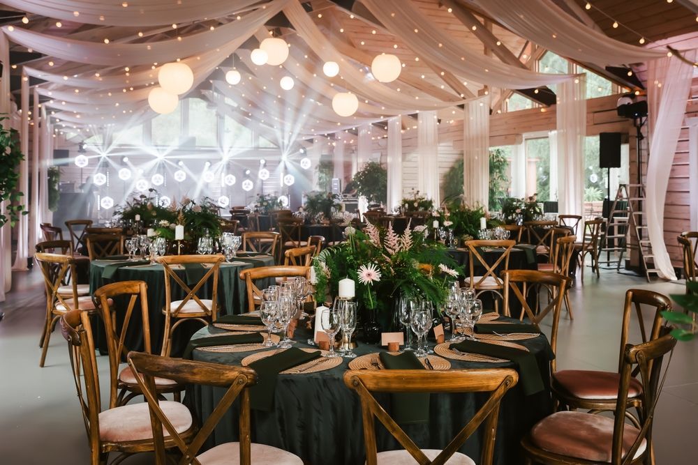Wedding reception hall with tables set for guests, draped with fabric and decorated with flowers.