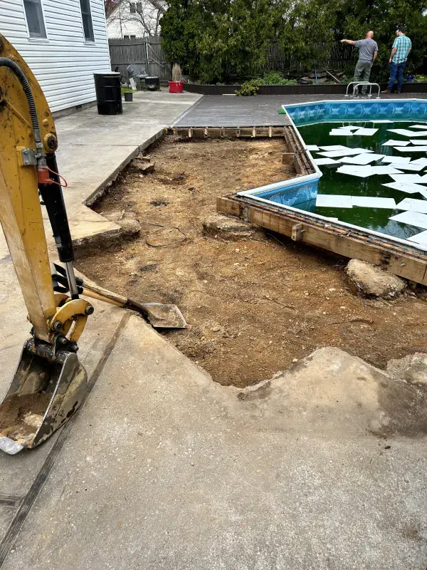 An excavator is digging a hole in the ground next to a swimming pool.