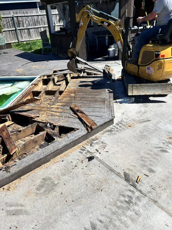 A man is driving a small excavator next to a swimming pool.