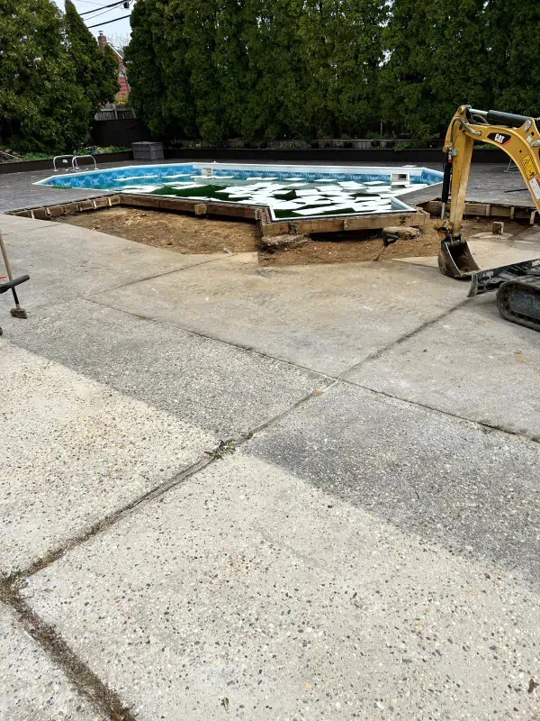 A yellow excavator is sitting in front of a swimming pool.