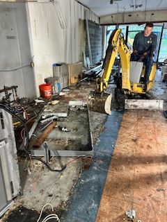 A man is riding a small excavator in a messy room.