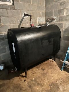 A black oil tank is sitting in a basement next to a ladder.