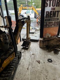 A small excavator is sitting in front of a store for rent sign.