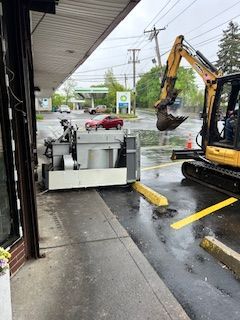 A yellow excavator is digging a hole in a parking lot.